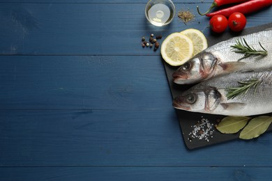 Photo of Flat lay composition with tasty sea bass fish and ingredients on blue wooden table. Space for text