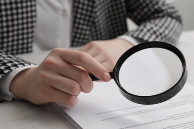 Woman looking at document through magnifier at white wooden table, closeup. Searching concept