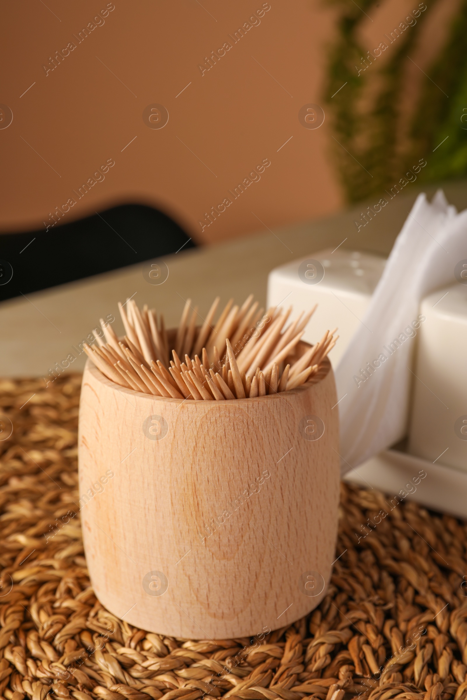 Photo of Wooden holder with many toothpicks on wicker mat, closeup