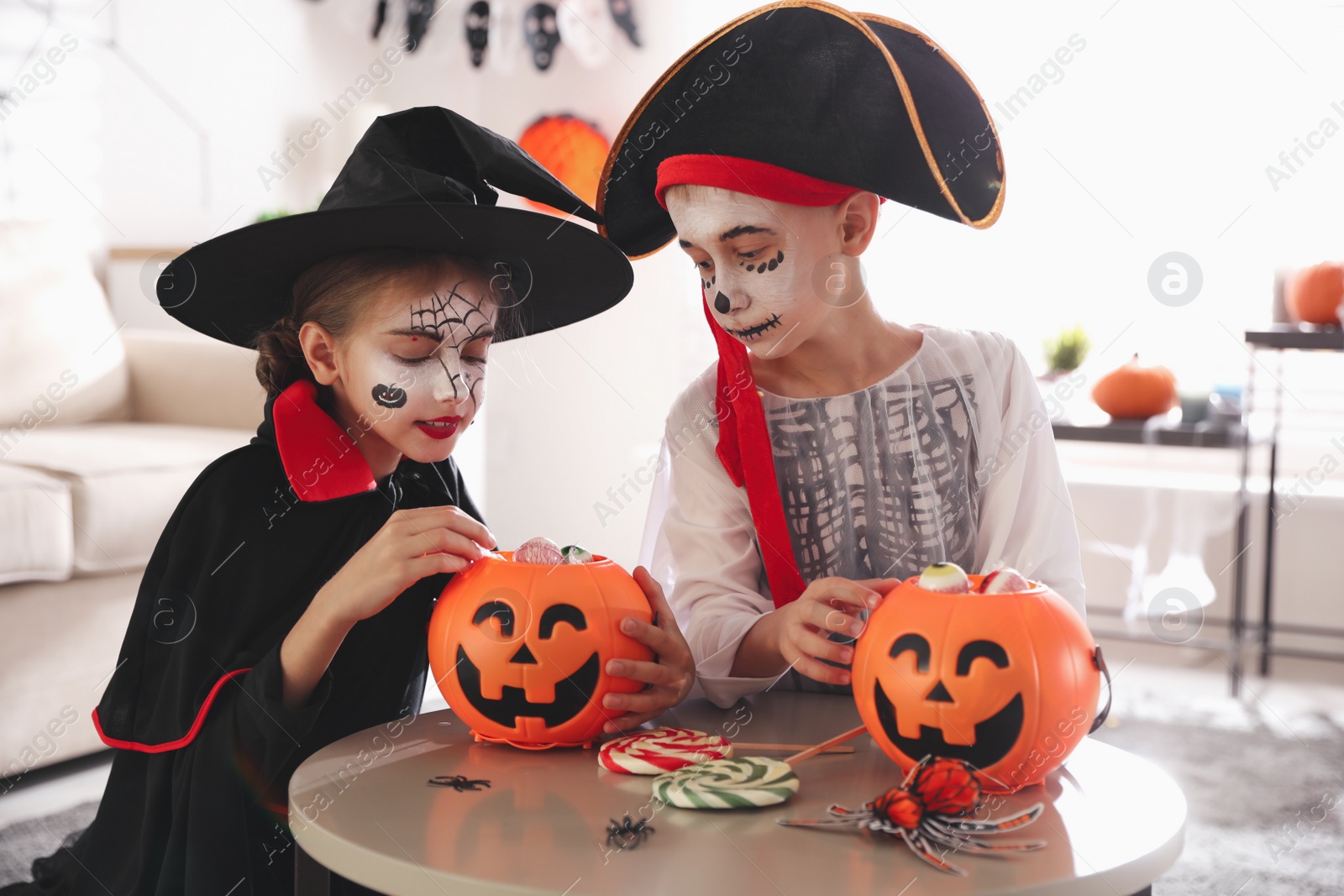 Photo of Cute little kids with pumpkin candy buckets wearing Halloween costumes at home