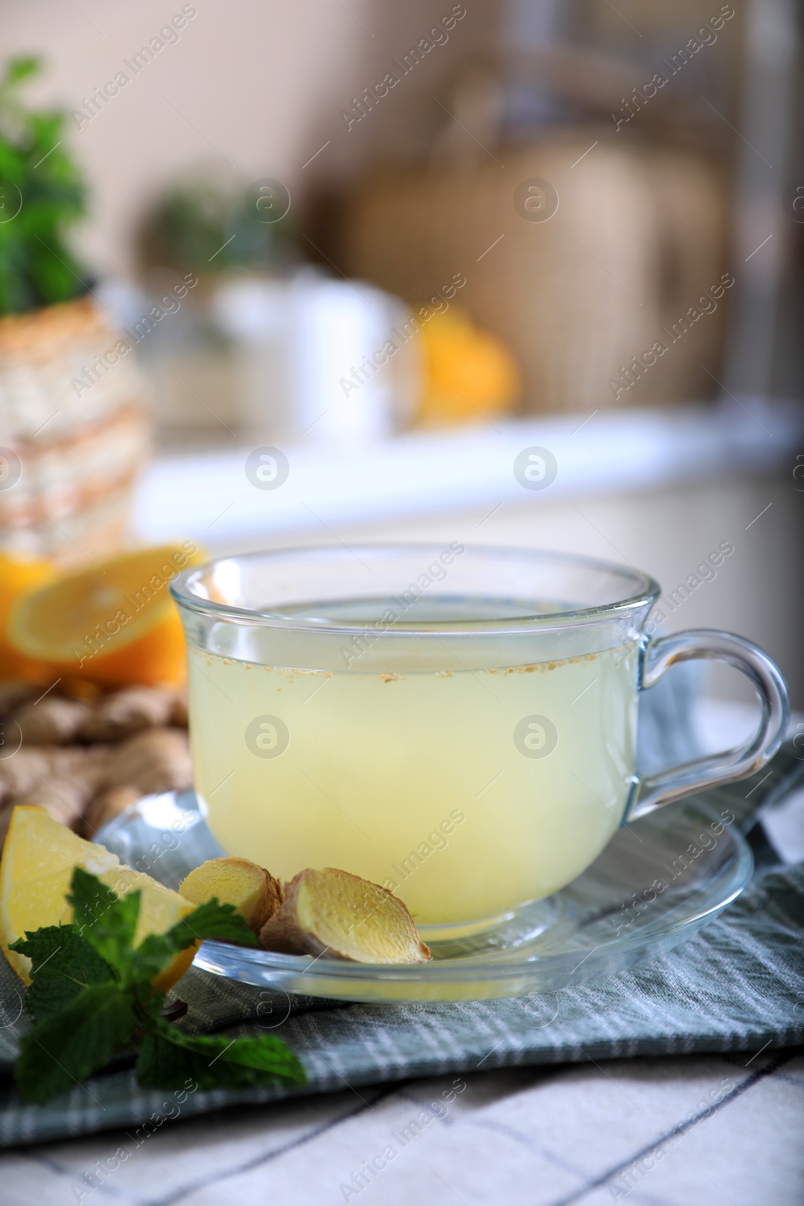 Photo of Glass of aromatic ginger tea and ingredients on white checkered tablecloth indoors