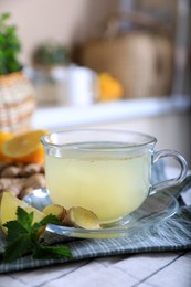Photo of Glass of aromatic ginger tea and ingredients on white checkered tablecloth indoors