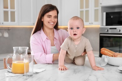 Photo of Happy young woman and her cute little baby spending time together in kitchen