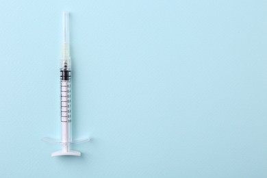 Photo of Cosmetology. Medical syringe on light blue background, top view. Space for text