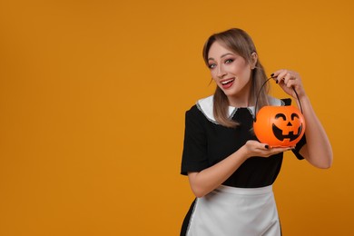 Happy woman in scary maid costume with pumpkin bucket on orange background, space for text. Halloween celebration