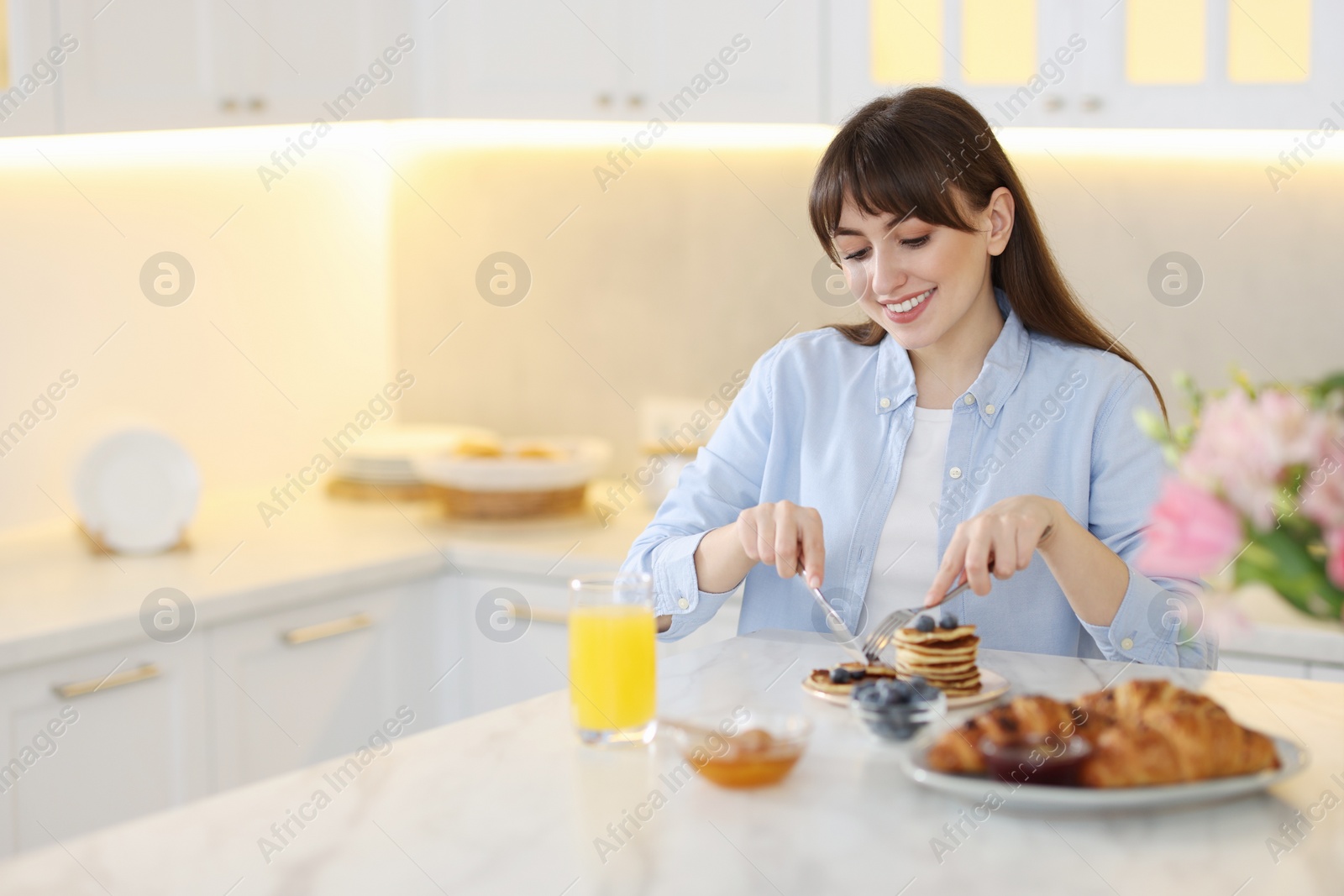 Photo of Smiling woman eating tasty pancakes at breakfast indoors. Space for text