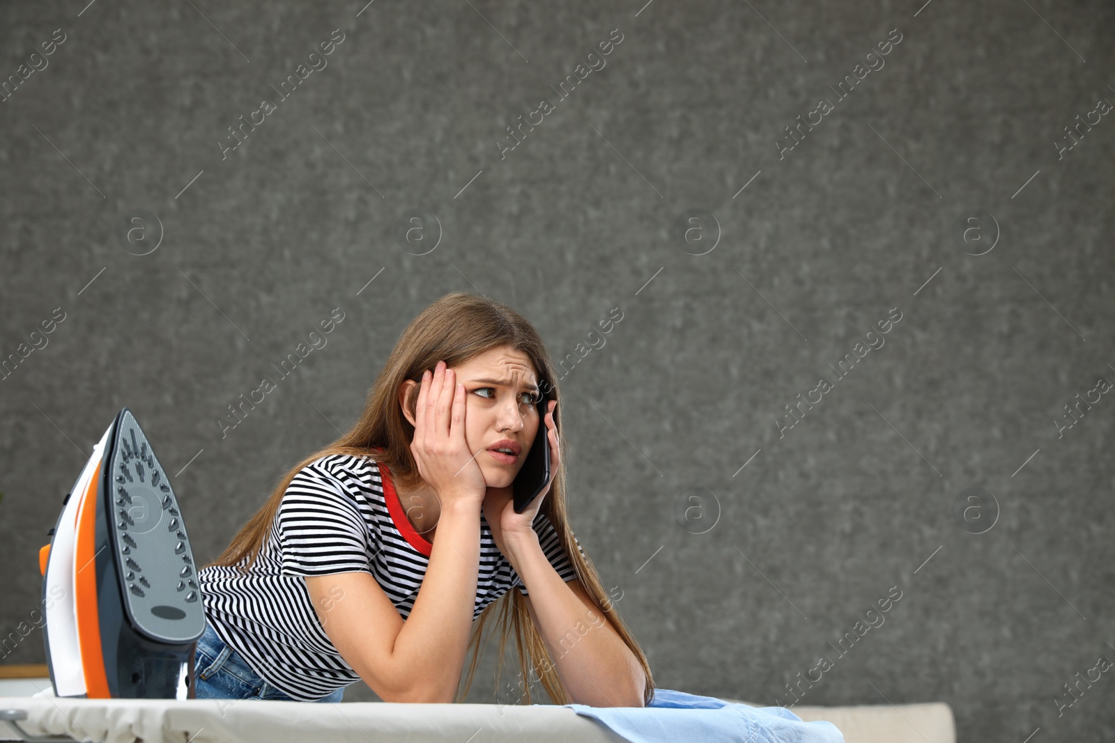 Photo of Emotional woman talking on phone while ironing clothes at home. Space for text