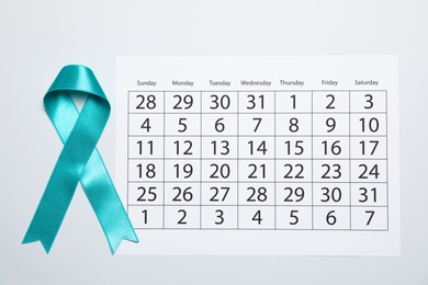 Photo of Teal awareness ribbon and calendar on white background, top view. Symbol of social and medical issues