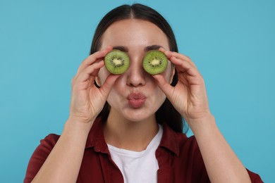 Photo of Woman covering eyes with halves of kiwi on light blue background