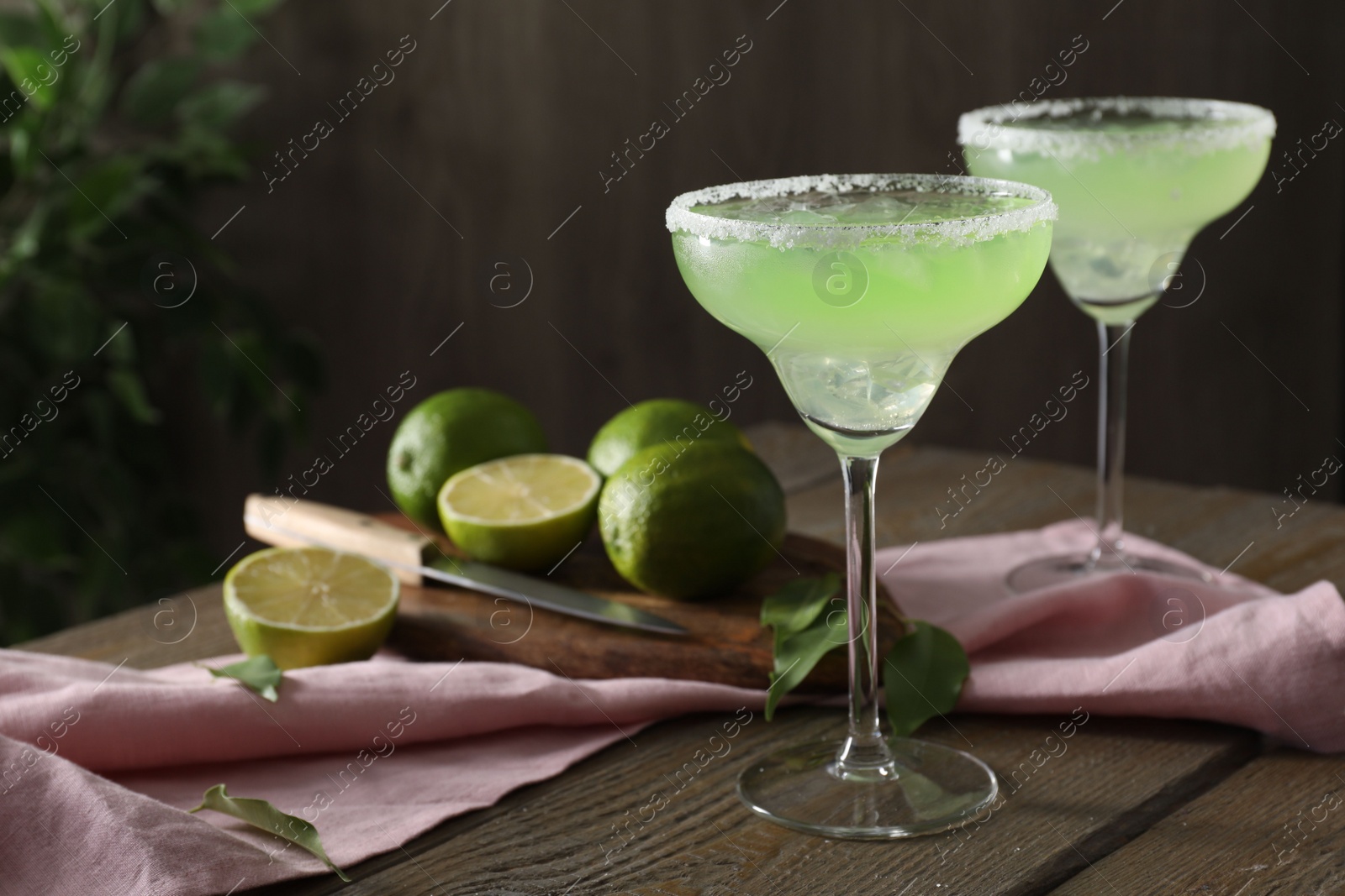 Photo of Delicious Margarita cocktail in glasses, lime and leaves on wooden table, closeup