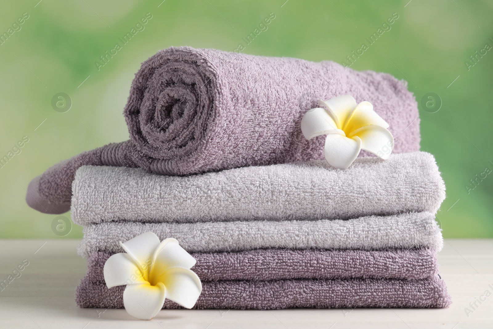 Photo of Soft folded towels and plumeria flowers on white wooden table