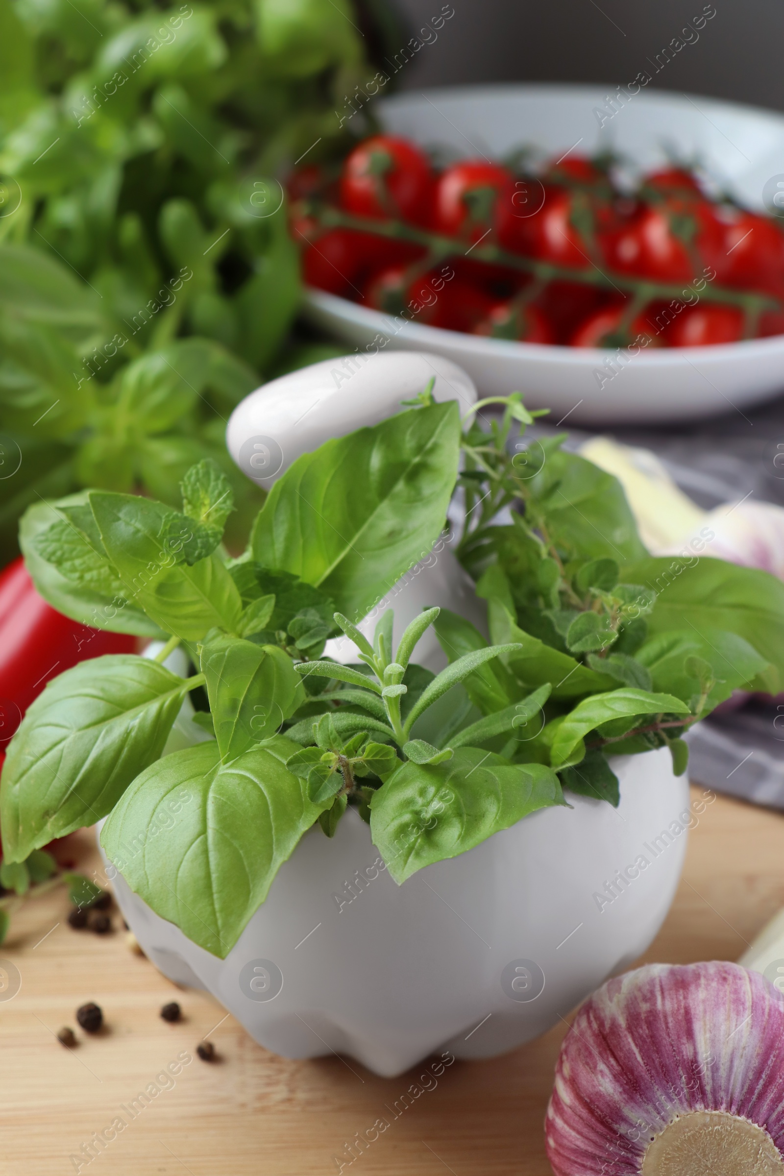 Photo of Mortar with fresh herbs, garlic and black peppercorns on wooden table, closeup