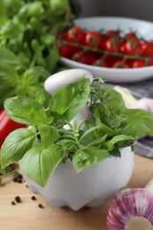 Photo of Mortar with fresh herbs, garlic and black peppercorns on wooden table, closeup