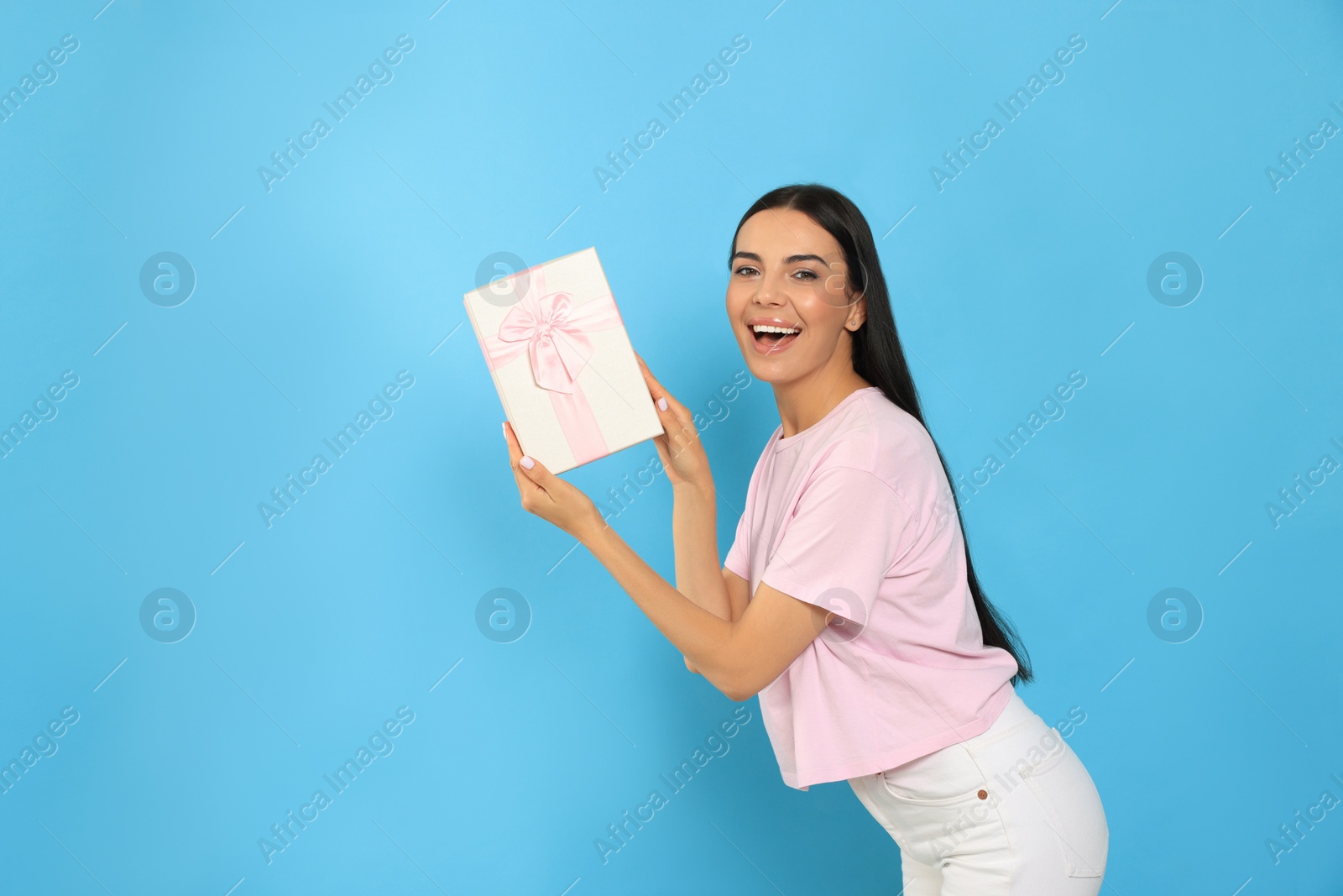 Photo of Happy young woman holding gift box on light blue background