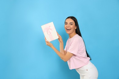 Happy young woman holding gift box on light blue background
