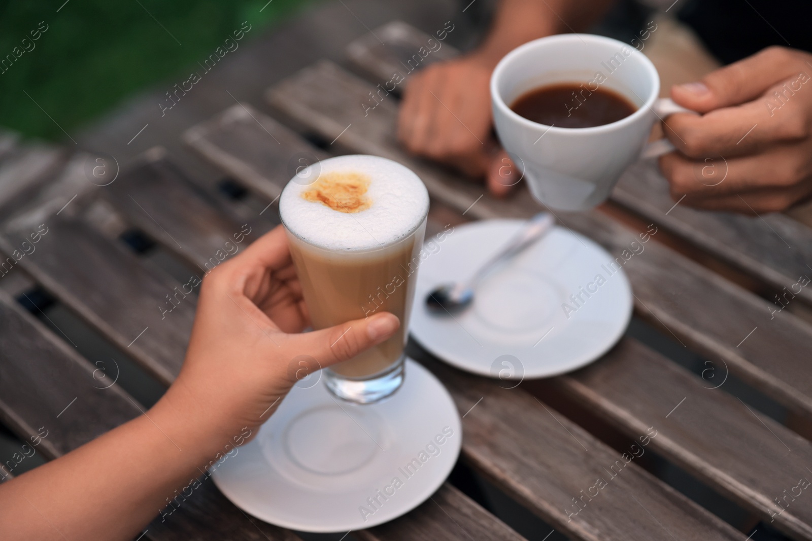 Photo of Man and woman drinking coffee at wooden table in outdoor cafe, closeup