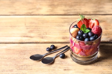 Photo of Delicious acai dessert with granola and berries in glass on wooden table. Space for text