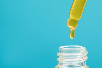 Photo of Dripping yellow serum from pipette into bottle on light blue background, closeup. Space for text