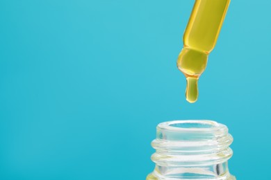 Dripping yellow serum from pipette into bottle on light blue background, closeup. Space for text