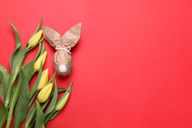 Photo of Easter bunny made of kraft paper and egg near beautiful tulips on red background, flat lay. Space for text