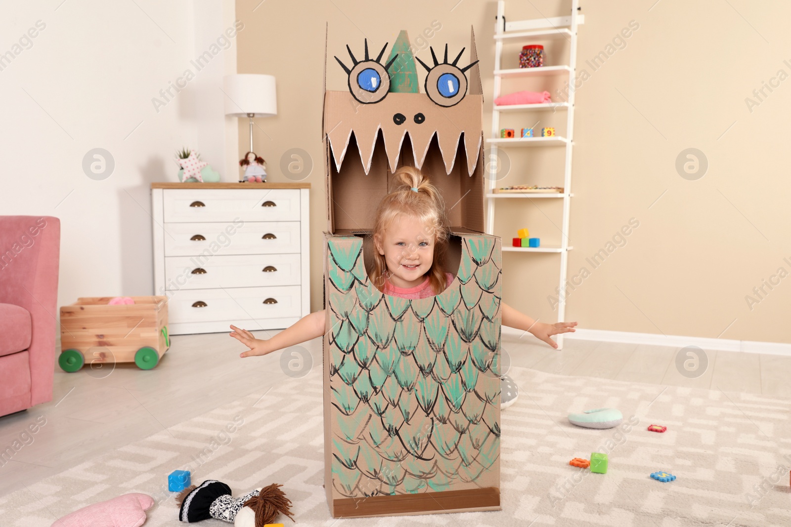 Photo of Cute little girl playing with cardboard dragon at home