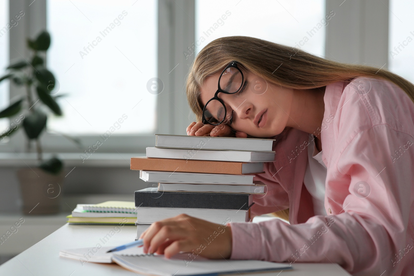 Photo of Young tired woman sleeping near books at white table in room