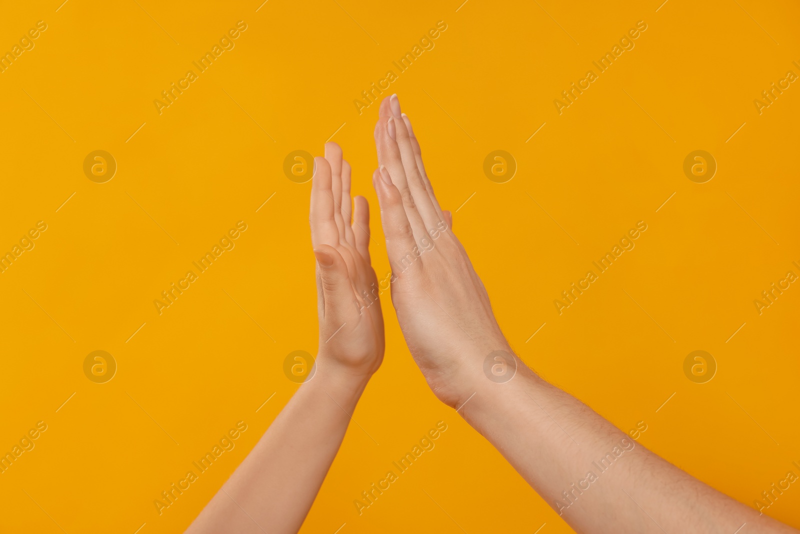 Photo of Mother and daughter giving high five on orange background, closeup of hands