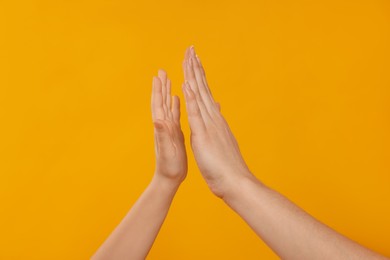 Photo of Mother and daughter giving high five on orange background, closeup of hands