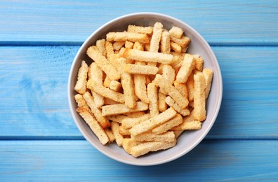 Crispy wheat rusks in bowl on light blue wooden table, top view