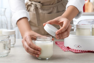 Photo of Woman with glass jar of fresh tasty yogurt at white wooden table in kitchen, closeup