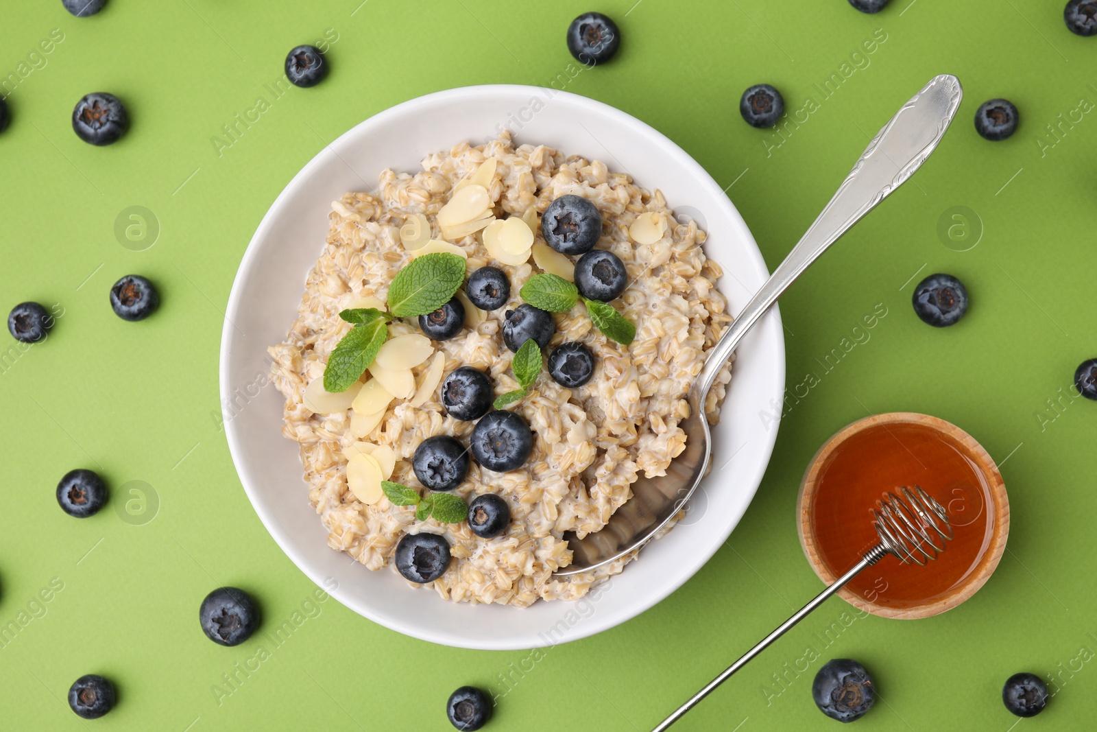 Photo of Tasty oatmeal with blueberries, mint and almond petals in bowl on light green background, flat lay