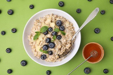 Photo of Tasty oatmeal with blueberries, mint and almond petals in bowl on light green background, flat lay