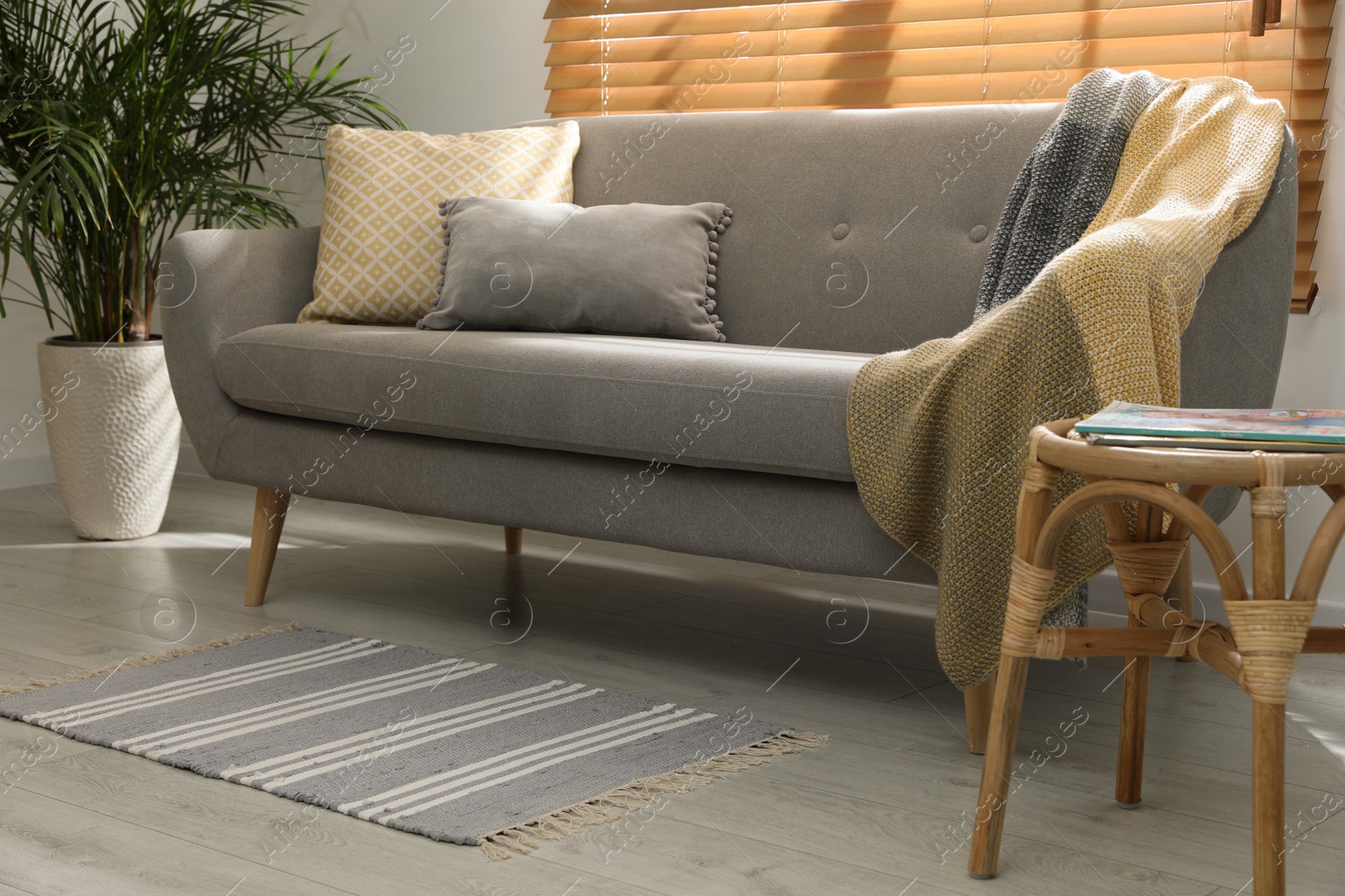 Photo of Stylish striped rug with fringe and comfortable sofa in living room. Interior design