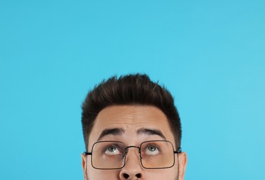 Photo of Man in glasses looking up on turquoise background, closeup