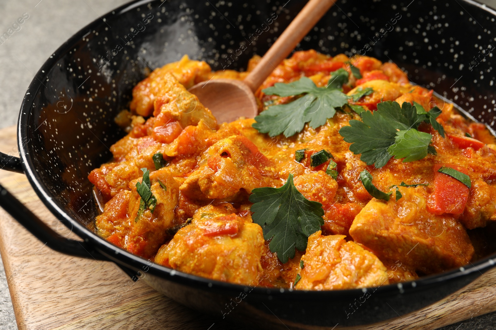 Photo of Delicious chicken curry in frying pan and spoon on table, closeup