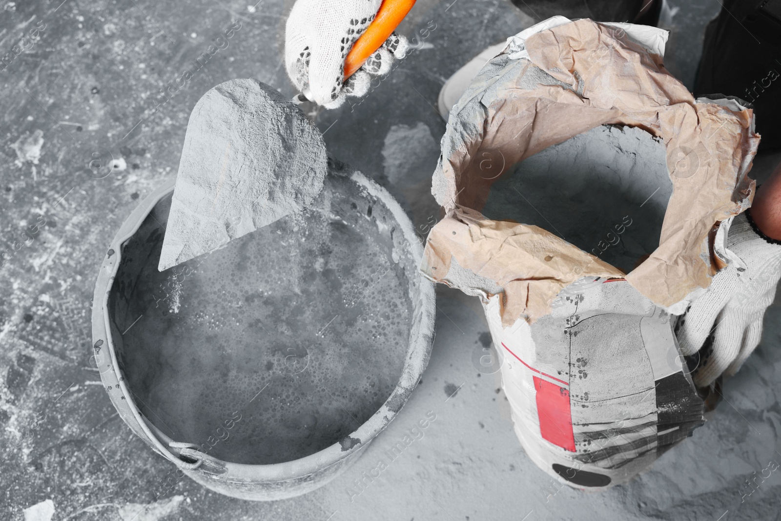 Photo of Worker with cement powder and trowel mixing concrete in bucket indoors, closeup