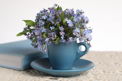 Beautiful forget-me-not flowers in cup, book and crochet tablecloth on table against white background, closeup