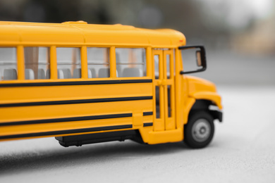 Photo of Yellow toy school bus against blurred background, closeup. Transport for students