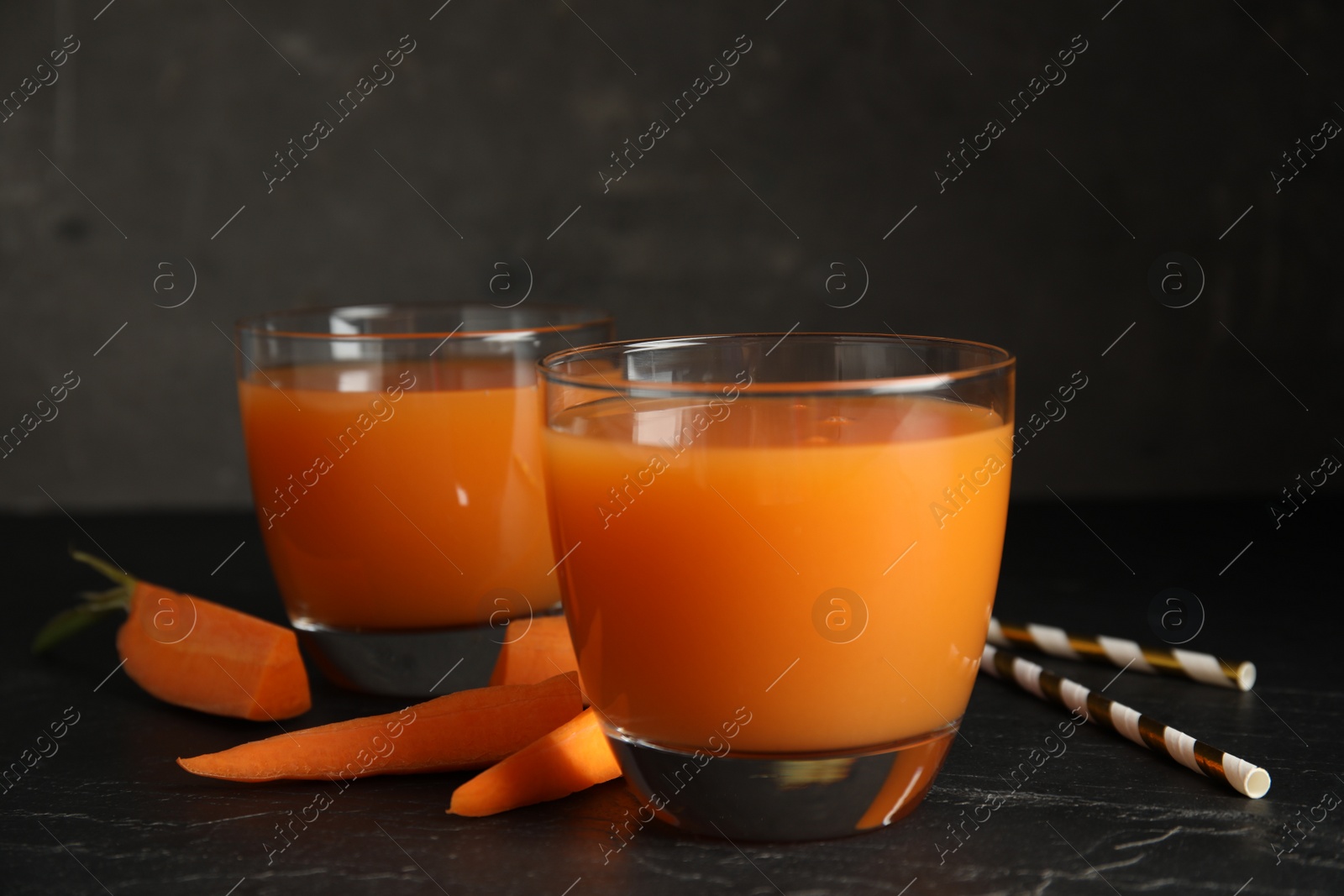 Photo of Glasses of freshly made carrot juice on black table