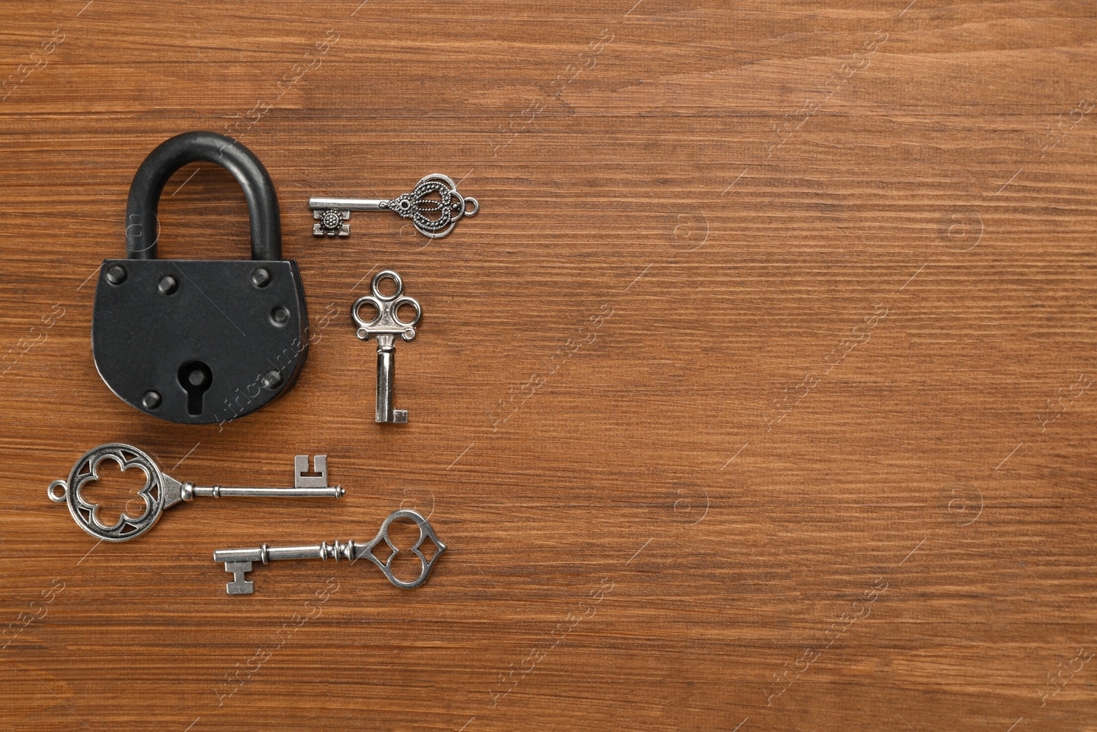 Photo of Padlock and beautiful vintage keys on wooden table, flat lay. Space for text