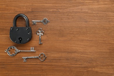 Padlock and beautiful vintage keys on wooden table, flat lay. Space for text