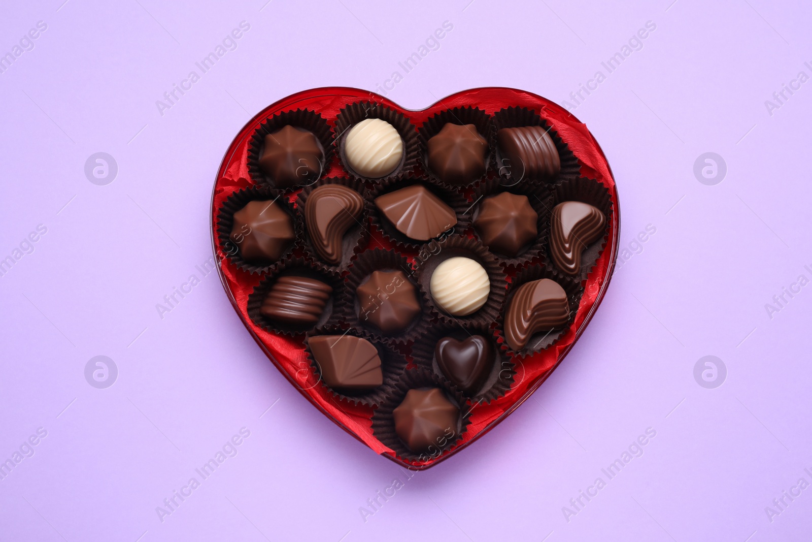 Photo of Heart shaped box with delicious chocolate candies on lilac background, top view