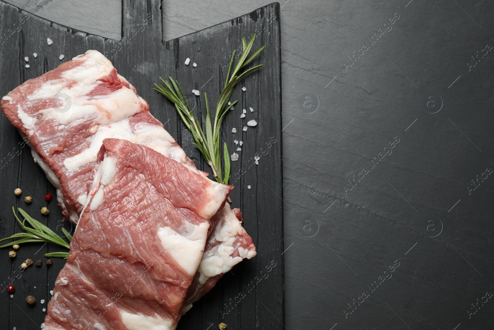 Photo of Raw ribs with rosemary and spices on black table, top view