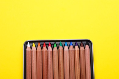 Photo of Box with many colorful pastel pencils on yellow background, top view and space for text. Drawing supplies