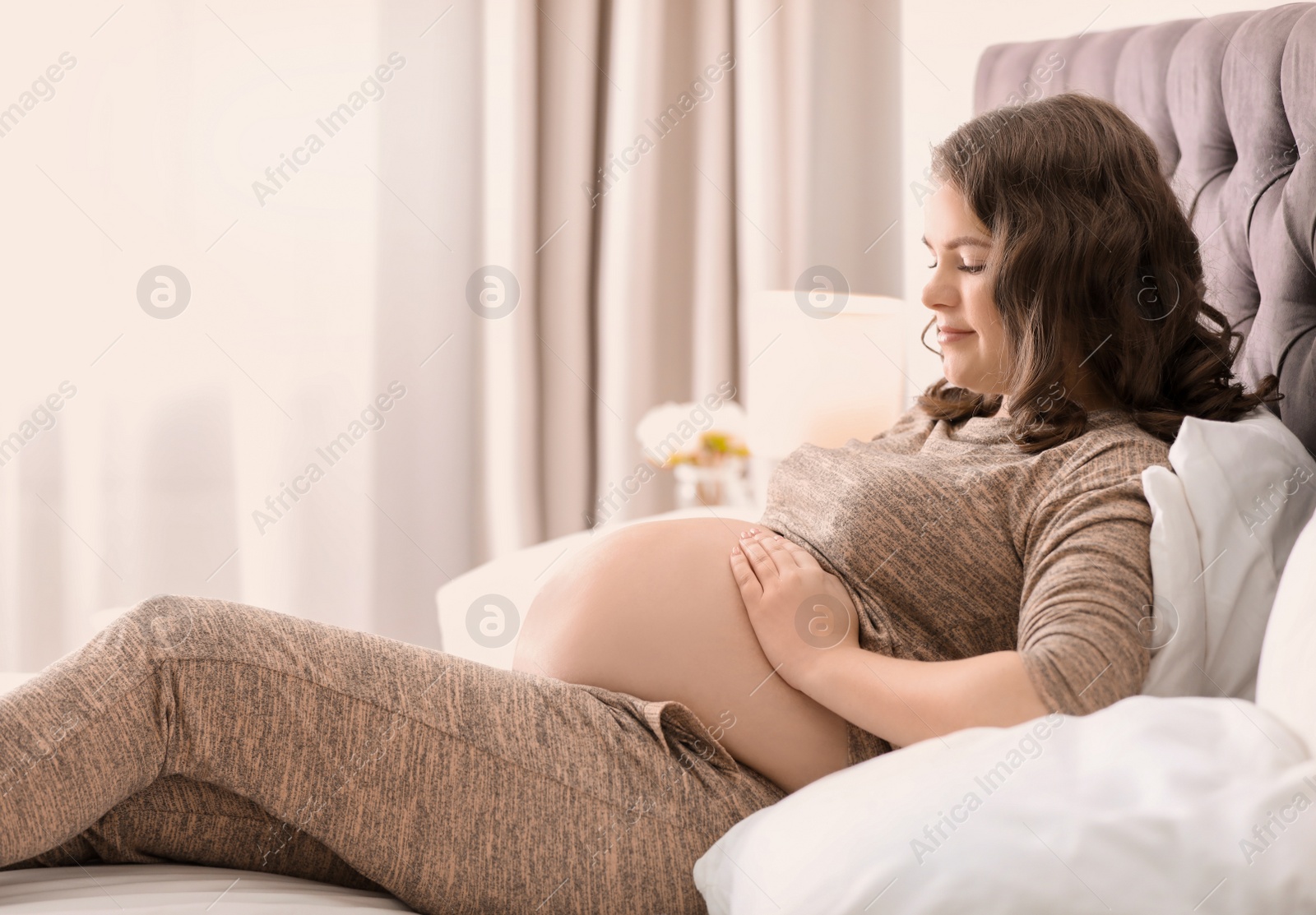 Photo of Young pregnant woman lying on bed at home