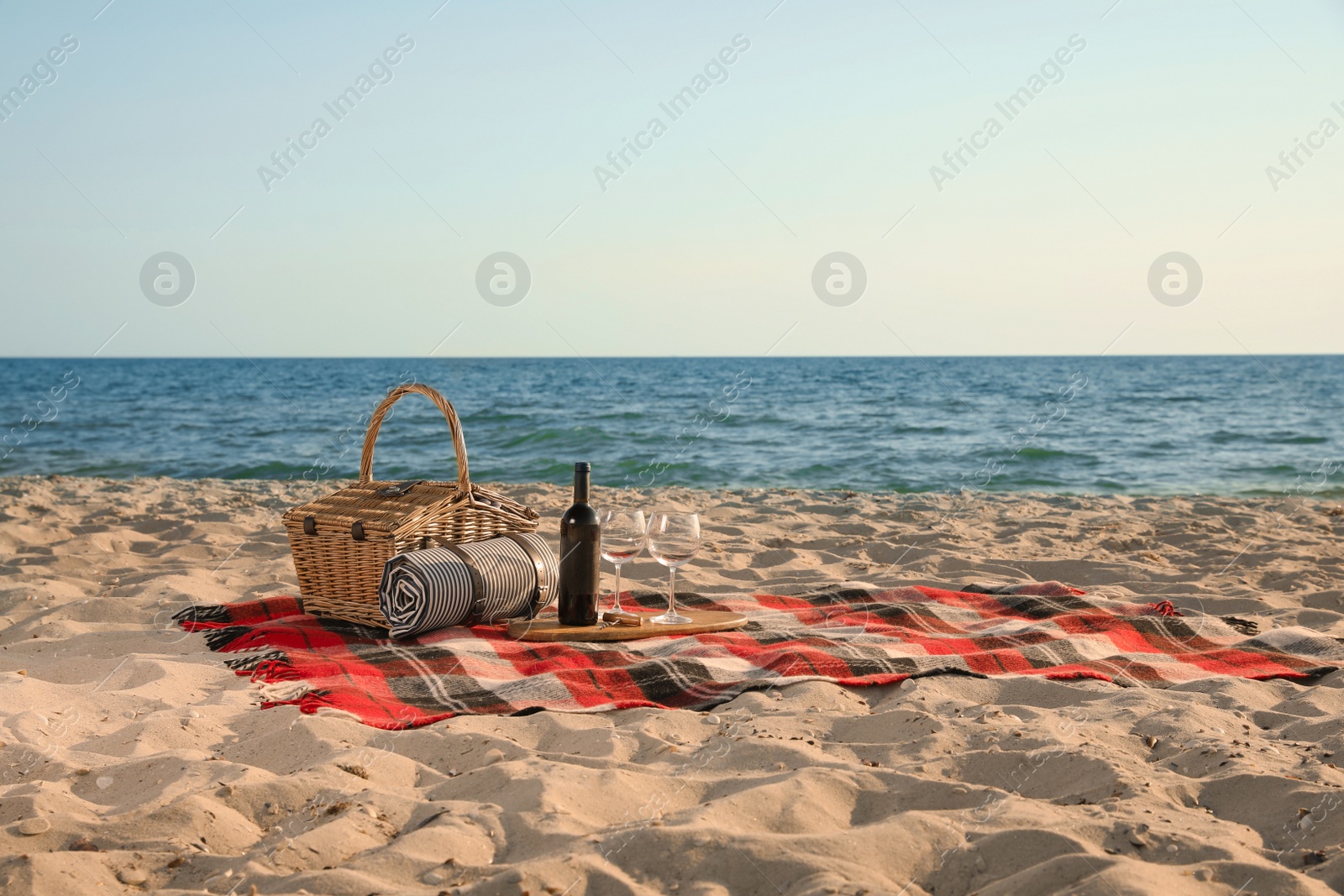 Photo of Blanket with picnic basket, bottle of wine and glasses on sandy beach near sea, space for text