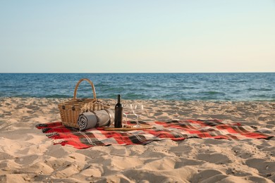 Photo of Blanket with picnic basket, bottle of wine and glasses on sandy beach near sea, space for text