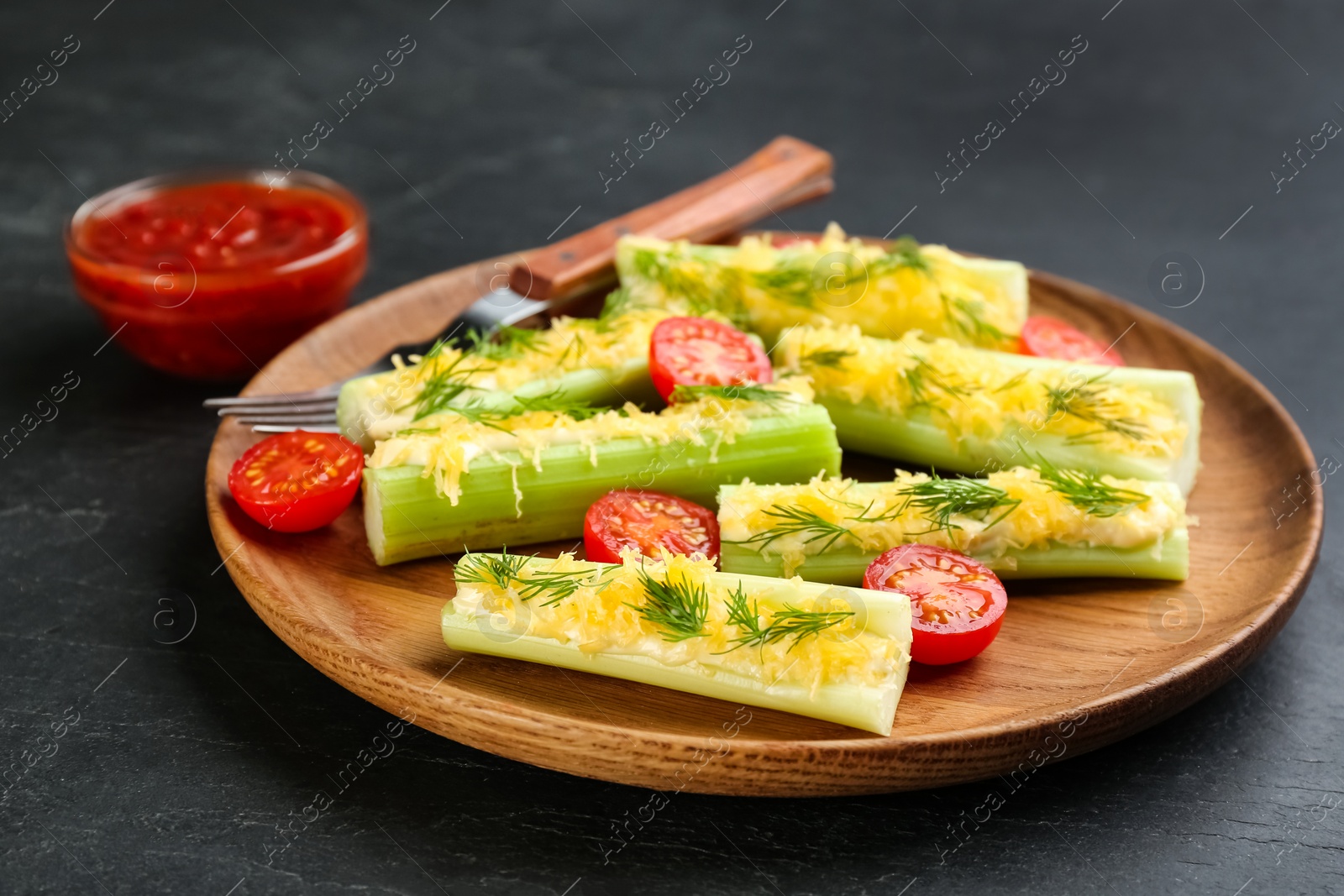 Photo of Celery sticks with sauce, cheese and tomatoes on black table, closeup