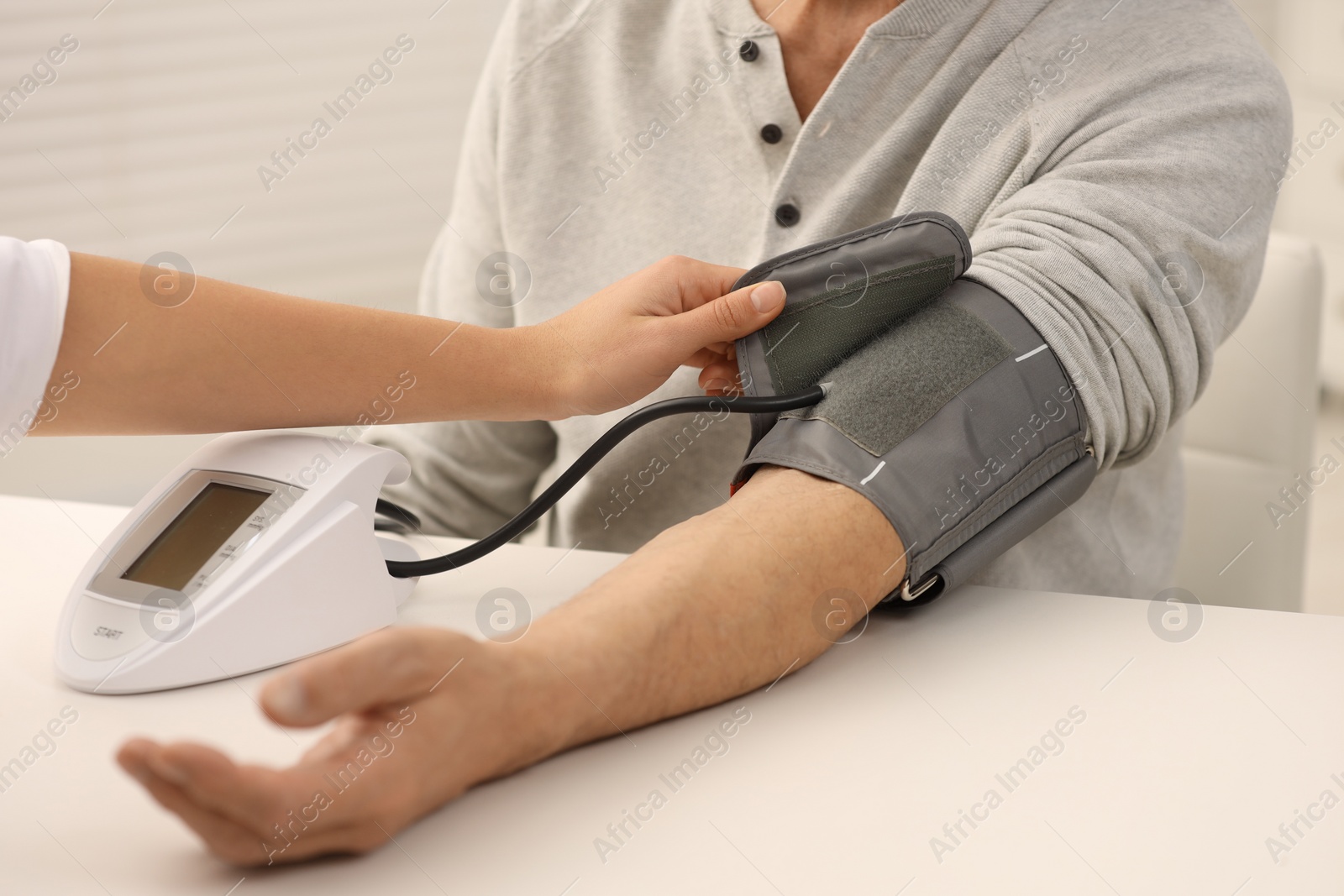Photo of Nurse measuring elderly patient's blood pressure at white table indoors, closeup