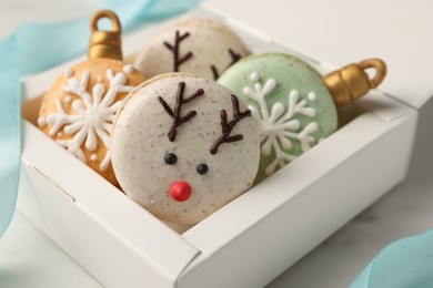 Photo of Beautifully decorated Christmas macarons in box and ribbon on white table, closeup